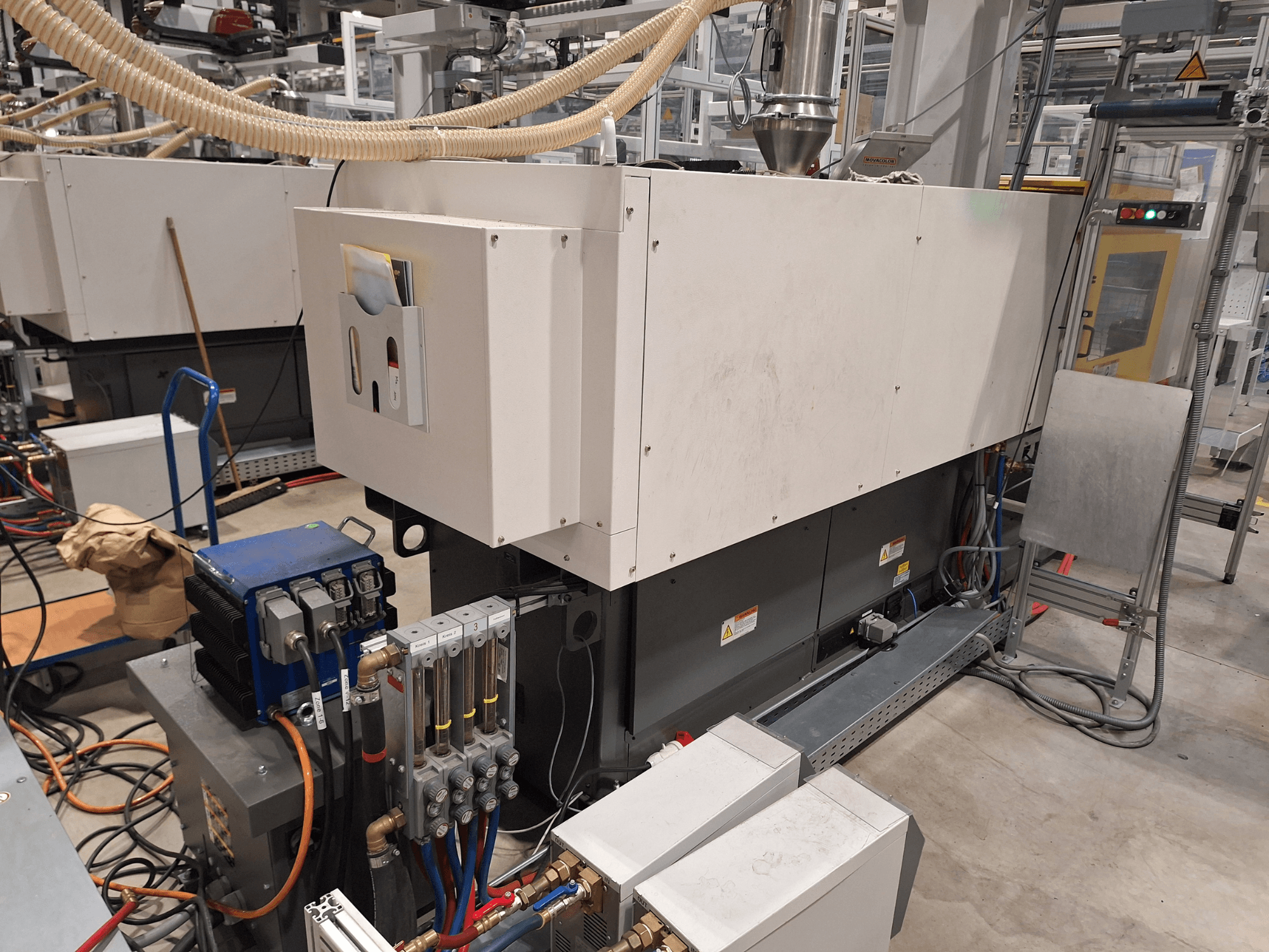 Industrijska oprema u tvorničkom okruženju; uključuje veliki stroj s upravljačkom pločom, crijevima i električnim priključcima, bočni pogled.