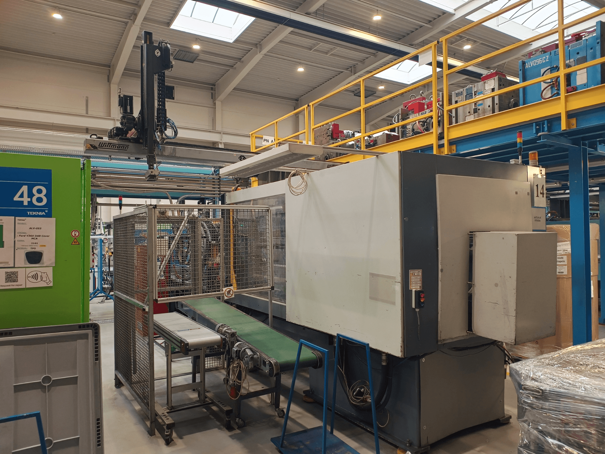 Industrijska automatizacijska oprema sa zelenim transporterom, označenim s '48', i nadzemnom dizalicom; bočni pogled na stroj na tvorničkom podu.